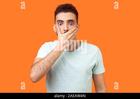 Je ne dirai pas. Portrait de peur d'intimidation homme en blanc T-shirt couvrant la bouche avec la main, à la peur de choqué les yeux, garder secret tabou. Banque D'Images