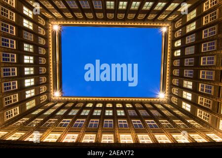 Vue depuis une cour intérieure d'un immeuble de bureaux avec de nombreuses fenêtres illuminées jusqu'à blue sky Banque D'Images