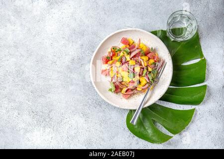 Hawaiian Tropical thon salade de mangue de tahiti sur plaque blanche on tropical monstera leafe Banque D'Images