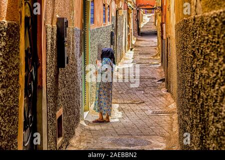 Femme parlant arabe dans le caractéristique ruelle de Médina de Marrakech, avec son voisin invisible derrière la porte. Banque D'Images