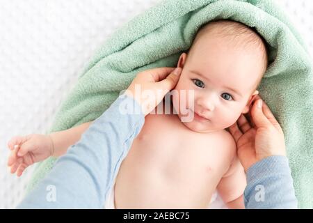 Massage du visage de bébé. Caressant doucement la mère bébé garçon visage avec les deux mains. Close up cropped shot. Sourire de bébé au cours de massage du visage. Banque D'Images