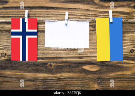 Drapeaux suspendus de la Norvège et l'Ukraine attache à la corde avec des pinces à linge avec de l'espace de copie sur papier blanc sur fond de bois.Les relations diplomatiques b Banque D'Images