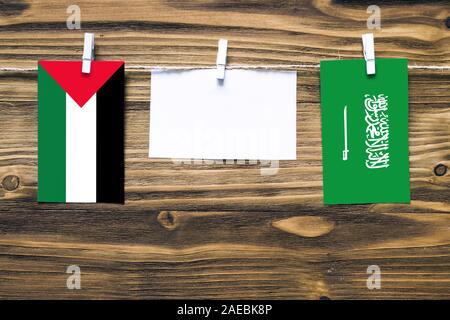 Drapeaux suspendus de la Palestine et l'Arabie saoudite attache à corde avec pinces à linge avec de l'espace de copie sur papier blanc sur fond de bois.rel diplomatique Banque D'Images