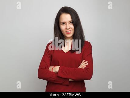 Belle jeune fille européenne se tient droit avec les bras croisés portant une croix en coton rouge deep v-neck sweater sur un fond gris. Banque D'Images