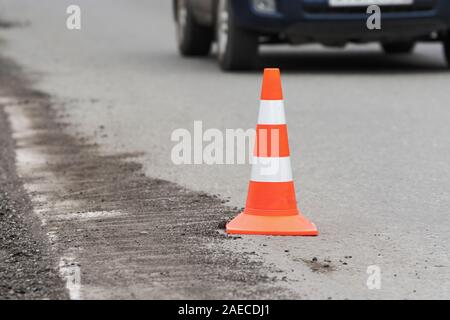 Cône de circulation routière d'avertissement situé sur la rue asphaltée route au cours de la réparation de routes en asphalte, travaille sur l'autoroute de l'automobile. Méconnaissable automobile dr Banque D'Images