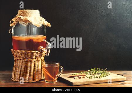 Des Kombucha fermenté boisson au pot avec robinet et dans la tasse sur fond sombre. Banque D'Images