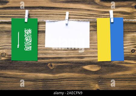 Drapeaux suspendus de l'Arabie Saoudite et l'Ukraine attache à la corde avec des pinces à linge avec de l'espace de copie sur papier blanc sur fond de bois.relation diplomatique Banque D'Images