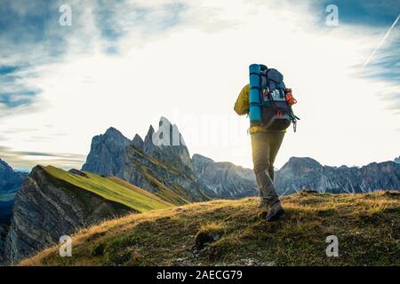 Jeune homme randonnée au sommet de la montagne de Seceda au lever du soleil. Sac à dos, veste jaune, bottes, bonnet. Voyageant à, puez Odle, Trentino Dolomites, Italie. Banque D'Images