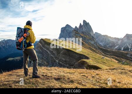 Jeune homme randonnée au sommet de la montagne de Seceda au lever du soleil. Sac à dos, veste jaune, bottes, bonnet. Voyageant à, puez Odle, Trentino Dolomites, Italie. Banque D'Images