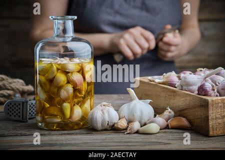 Huile aromatisée à l'ail ou de l'infusion aromatique bouteille caisse en bois et de gousses d'ail sur une table de cuisine en bois. Femme pèle l'ail avec un couteau sur backgrou Banque D'Images