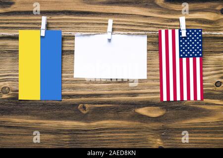 Drapeaux suspendus de l'Ukraine et de l'United States joint à la corde avec pinces à linge avec de l'espace de copie sur papier blanc sur fond de bois.rela diplomatique Banque D'Images