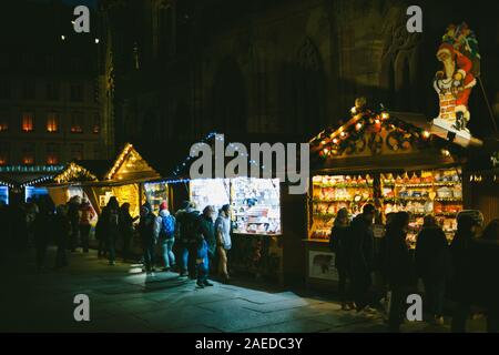 Strasbourg, France - Dec 20, 2016 : scène de nuit avec rangée de stalles du marché chalets avec plusieurs jouets à vendre à la place de la Cathedrale Notre-Dame de touristes admirant les habitants les cadeaux et jouets Banque D'Images