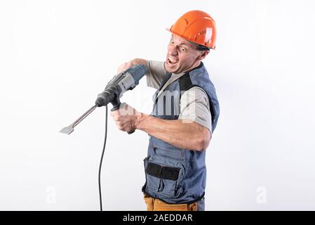 Un constructeur avec une drôle d'expression, dans un casque, avec une perceuse dans les mains. Banque D'Images