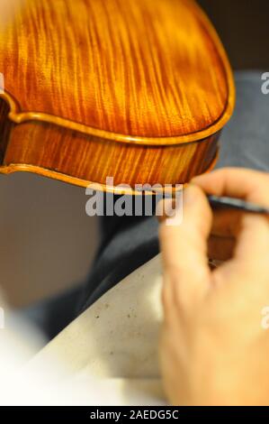 Maître luthier violon fabricant vernissage d'un luth à cordes de violon fait à la main comme touche finale pour terminer sa création dans son atelier de Cremona, Lombardie Banque D'Images