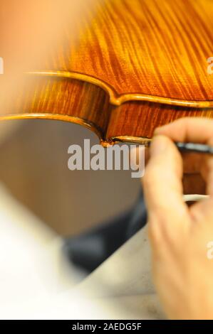 Maître luthier violon fabricant vernissage d'un luth à cordes de violon fait à la main comme touche finale pour terminer sa création dans son atelier de Cremona, Lombardie Banque D'Images