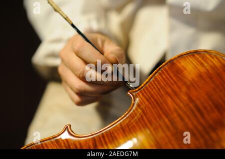 Maître luthier violon fabricant vernissage d'un luth à cordes de violon fait à la main comme touche finale pour terminer sa création dans son atelier de Cremona, Lombardie Banque D'Images