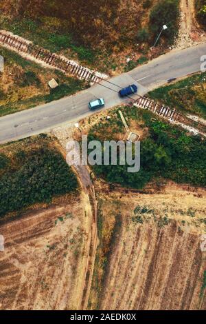 Vue aérienne de deux voitures qui passent sur le chemin de passage à niveau avec barrières de flèche relevée Banque D'Images