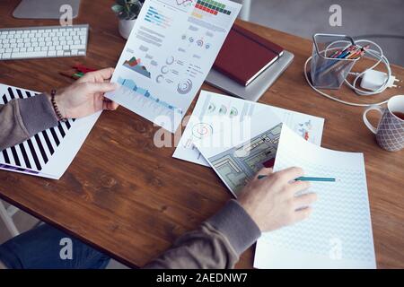 Gros plan du portrait moderne méconnaissable rapport statistique avec des données de couleur tout en travaillant au bureau dans un bureau en bois, copy space Banque D'Images