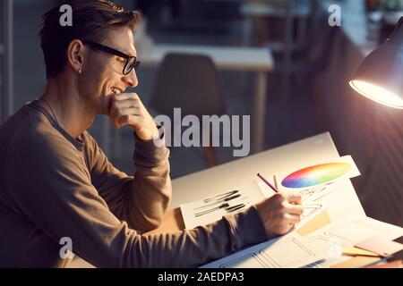 Vue de côté de l'homme portrait contemporain designer croquis dessin au bureau tout en travaillant en studio éclairé par la lumière de la lampe, copy space Banque D'Images