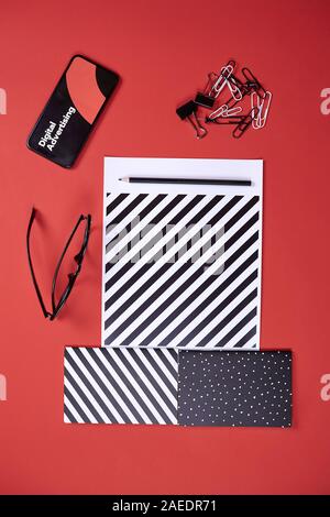 Concept de publicité numérique avec écran noir et blanc au milieu des textures bureau sur fond rouge, copy space Banque D'Images