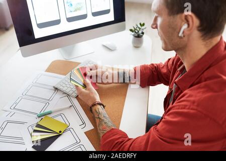 High angle portrait of tattooed man holding tout en choisissant des échantillons de couleurs de la palette de couleurs web design project, copy space Banque D'Images