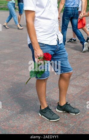 Un jeune homme avec une fleur dans la main est en attente d'un proche à venir. Une partie du corps d'un homme. L'été, sur la rue. Banque D'Images