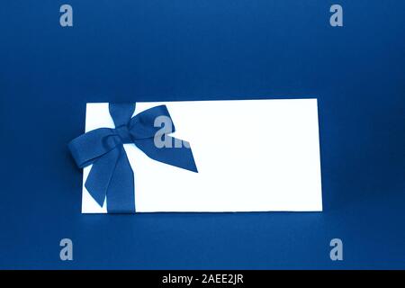 Carte cadeau blanc isolé avec ruban de couleur bleu très tendance noeud sur fond bleu. Couleur de l'année 2020 concept. Carte de vœux de concept. S COPIE Banque D'Images
