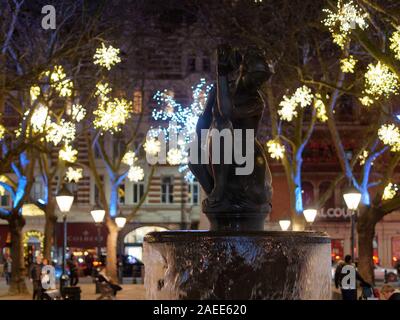 La silhouette de la fontaine avec une statue à l'égard des belles lumières de Noël dans l'arrière-plan à Sloan Square. Banque D'Images