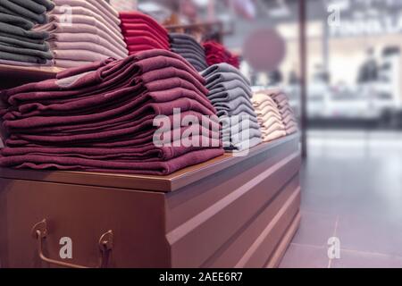 Les vêtements sont soigneusement empilés sur un présentoir en bois dans le magasin. pulls, pulls et chandails chauds de différentes couleurs sont rouge foncé et oth. Banque D'Images