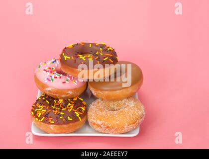 Petite plaque carrée avec donuts empilés, différentes saveurs. Fond rose avec copie espace. Banque D'Images