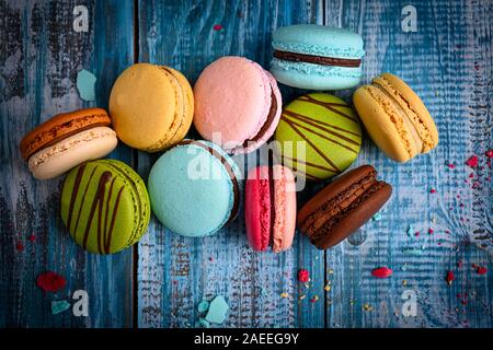 Superbe Photo d'un assortiment de macarons colorés et joliment disposées sur le dessus de table en bois bleu décoré de pétales de fleurs de mauve Banque D'Images