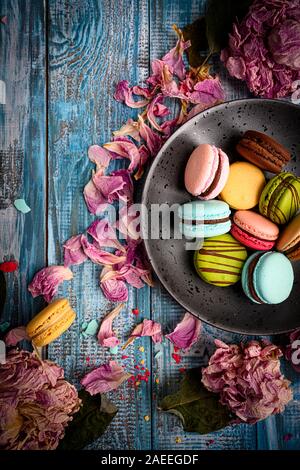 Superbe Photo d'un assortiment de macarons colorés et joliment disposées sur le dessus de table en bois bleu décoré de pétales de fleurs de mauve Banque D'Images