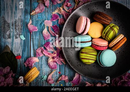 Superbe Photo d'un assortiment de macarons colorés et joliment disposées sur le dessus de table en bois bleu décoré de pétales de fleurs de mauve Banque D'Images