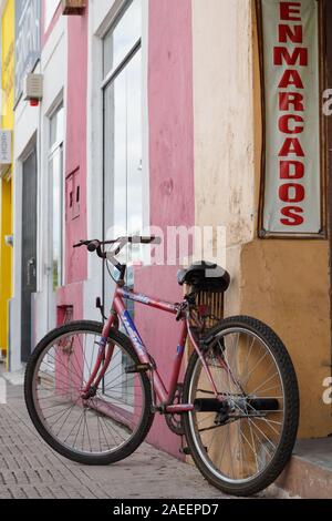 Un vélo rouge garée en passant par le bâtiment coloré dans le trottoir de Merida, Yucatan, Mexique. Banque D'Images