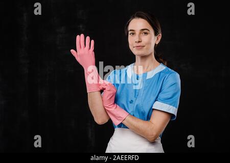 Joli hôtel maid putting sur rose gants en caoutchouc à l'avant de l'appareil photo Banque D'Images