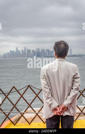 Monsieur âgé profitant de la vue tout en écoutant de la musique sur l'orange ferry de Staten Island à New York City à jour brumeux. Banque D'Images