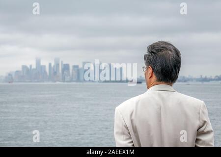Monsieur âgé profitant de la vue tout en écoutant de la musique sur l'orange ferry de Staten Island à New York City à jour brumeux. Banque D'Images