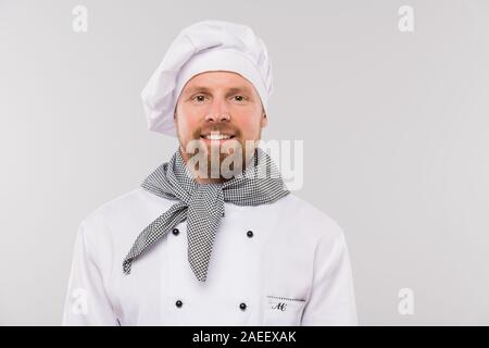 Jeunes chef barbu en uniforme vous regarde avec sourire à pleines dents Banque D'Images