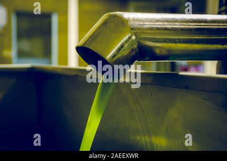 Huile d'olive extra vierge fraîchement pressée s'écoulant du tube vers le réservoir d'une usine industrielle d'huile d'olive. Banque D'Images