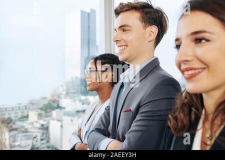 Heureux les jeunes de l'équipe entreprises multi-ethnique à la grande fenêtre du bureau par Banque D'Images