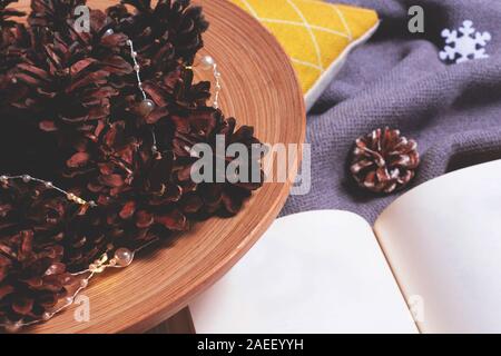 Composition de Noël avec livre ouvert avec l'hiver plaid douillet, les lumières de Noël en pommes de pin. Maison de vacances confort matin concept. Hygge style. Télévision lay, t Banque D'Images
