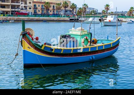 Un luzzu coloré près de la rive d'un village de pêcheurs sur une journée ensoleillée, à Malte. Le bateau de pêche en bleu et jaune est situé dans le port. Banque D'Images