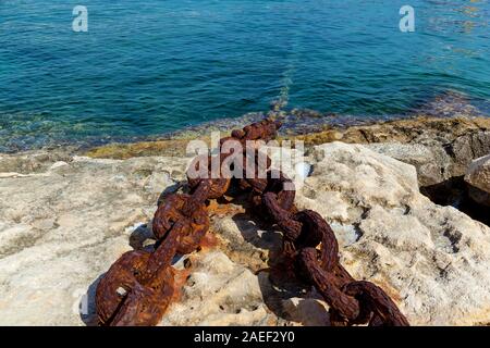 Vue rapprochée de bollard pierre avec une vieille chaîne rouillée sur le fond de l'eau bleu. Banque D'Images