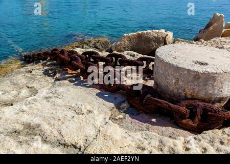 Vue rapprochée de bollard pierre avec une vieille chaîne rouillée sur le fond de l'eau bleu. Banque D'Images