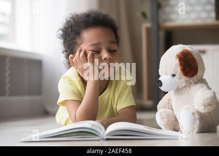 Ennuyer little boy reading book lying on floor Banque D'Images