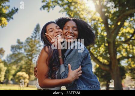 Portrait of a Smiling happy divers jeune femelle noir et blanc friends hugging les uns les autres et s'amuser en plein air dans le parc Banque D'Images