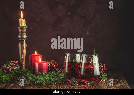 L'alimentation de vœux de Noël et du Nouvel An, la composition. Deux verres de boisson grenade entouré des branches de pins et de fête bougies, fond noir. Clo Banque D'Images