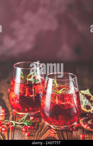 Deux verres de cocktail Grenade décorées avec du romarin et de la glace, le froid verre sur fond de béton bordeaux claret. Close up, faible profondeur du Banque D'Images