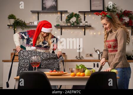 Deux jeunes femmes préparer la nourriture pour le Nouvel An dans la cuisine décorée avec des guirlandes et des couronnes de Noël. Banque D'Images