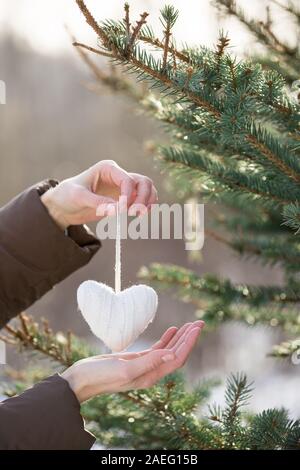 Close up of woman's hands decorating Christmas Tree avec coeur en tricot blanc à l'extérieur. Présente un décor et des éléments. Vacances d'hiver et de concept. Banque D'Images